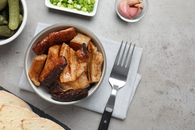 Photo of Bowl with tasty fried pork fatback slices on grey table, flat lay