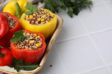 Photo of Quinoa stuffed bell peppers and parsley in baking dish on white tiled table, closeup. Space for text