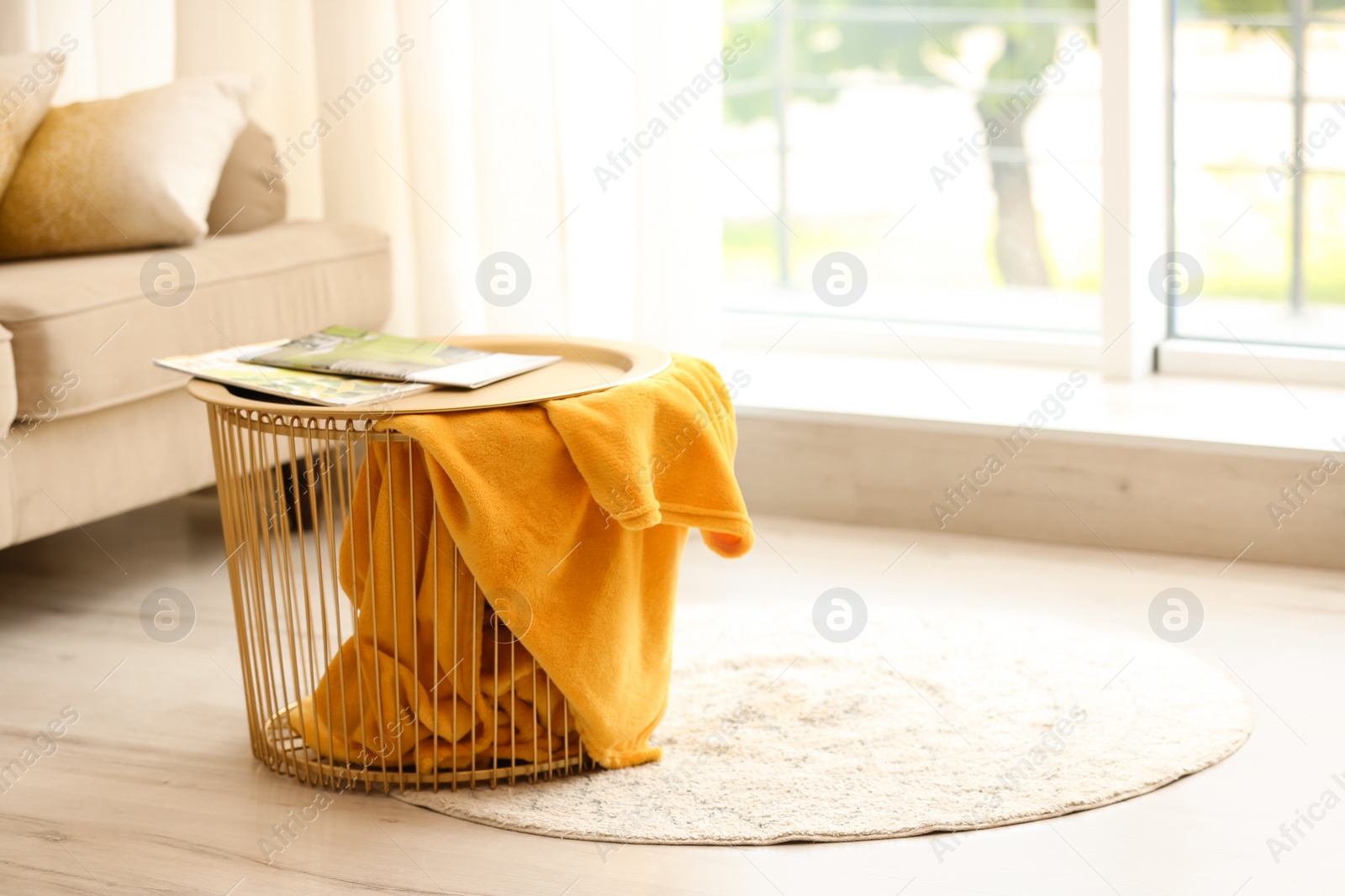 Photo of Metal basket with yellow blanket in modern room, space for text. Idea for interior design