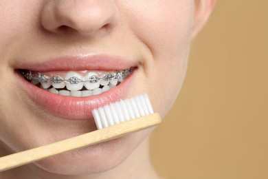 Photo of Woman with dental braces cleaning teeth on beige background, closeup