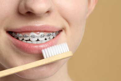 Woman with dental braces cleaning teeth on beige background, closeup