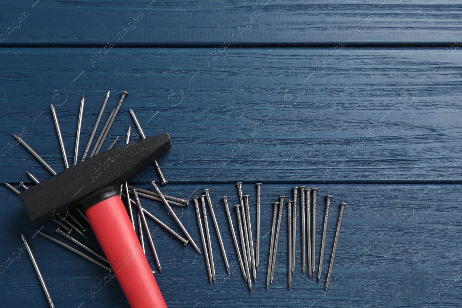 Photo of Hammer and metal nails on blue wooden table, flat lay. Space for text