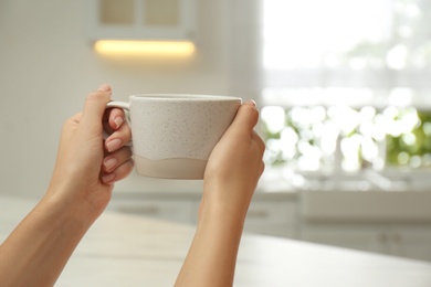 Woman holding elegant cup in kitchen, closeup