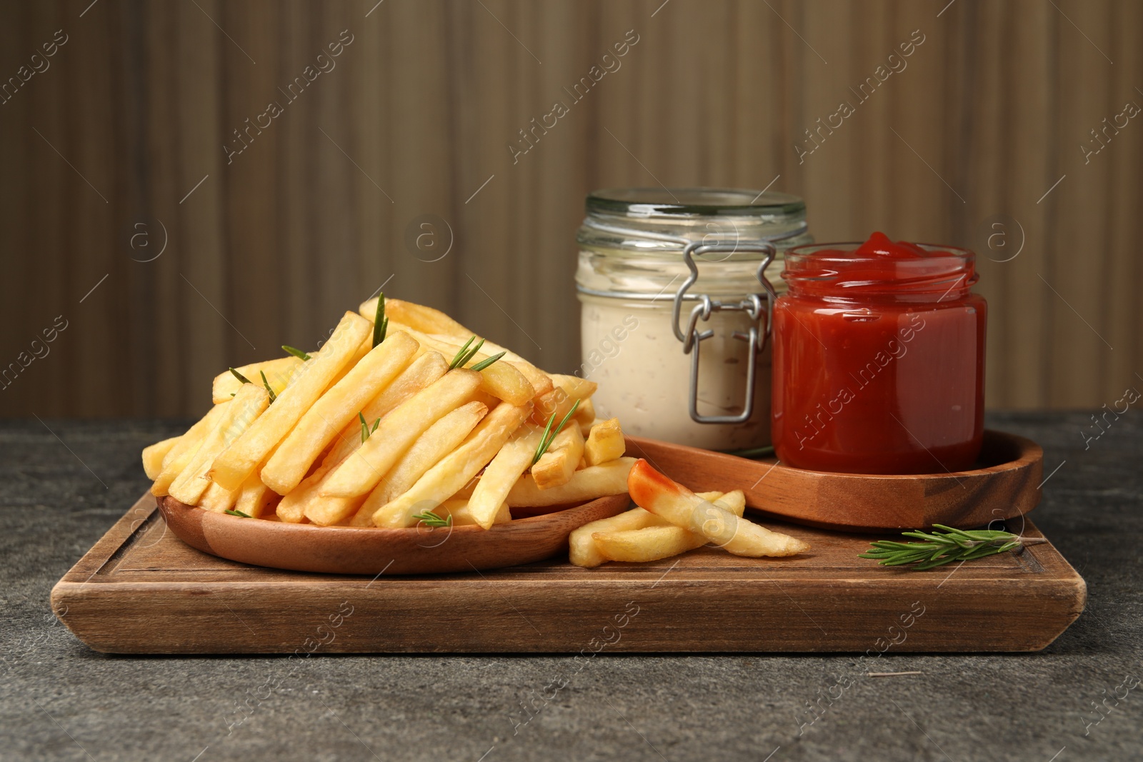 Photo of Delicious french fries served with sauces on grey textured table