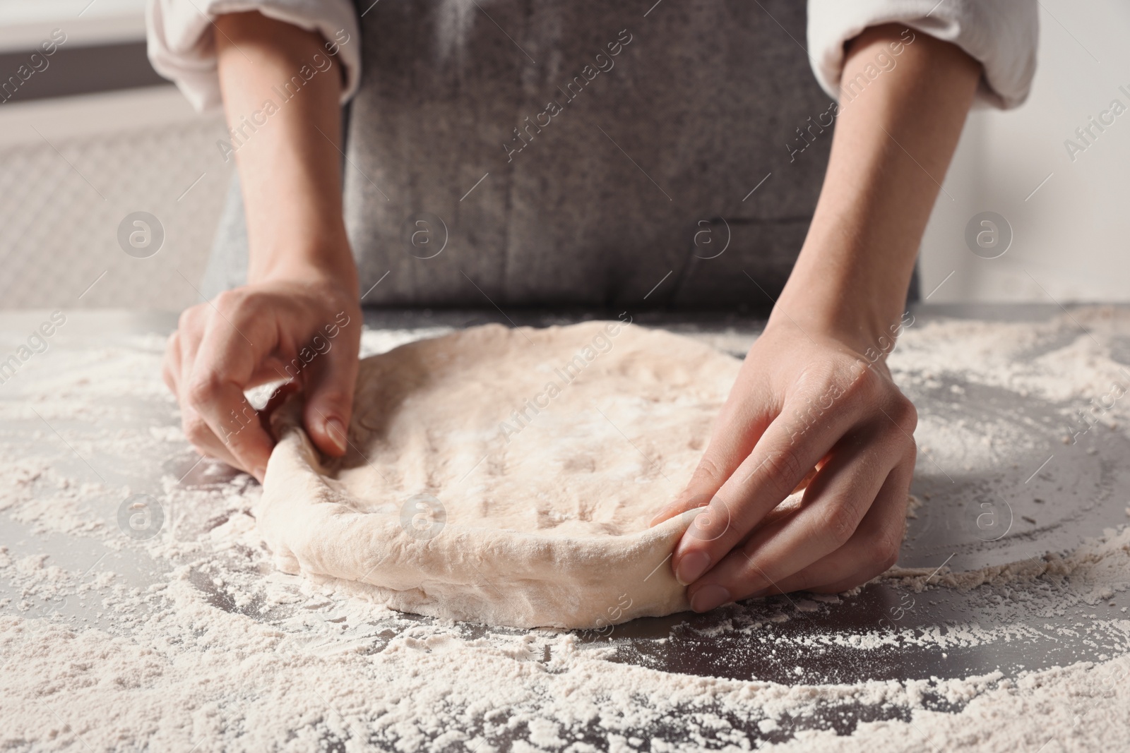 Photo of Woman kneading dough at table in kitchen, closeup