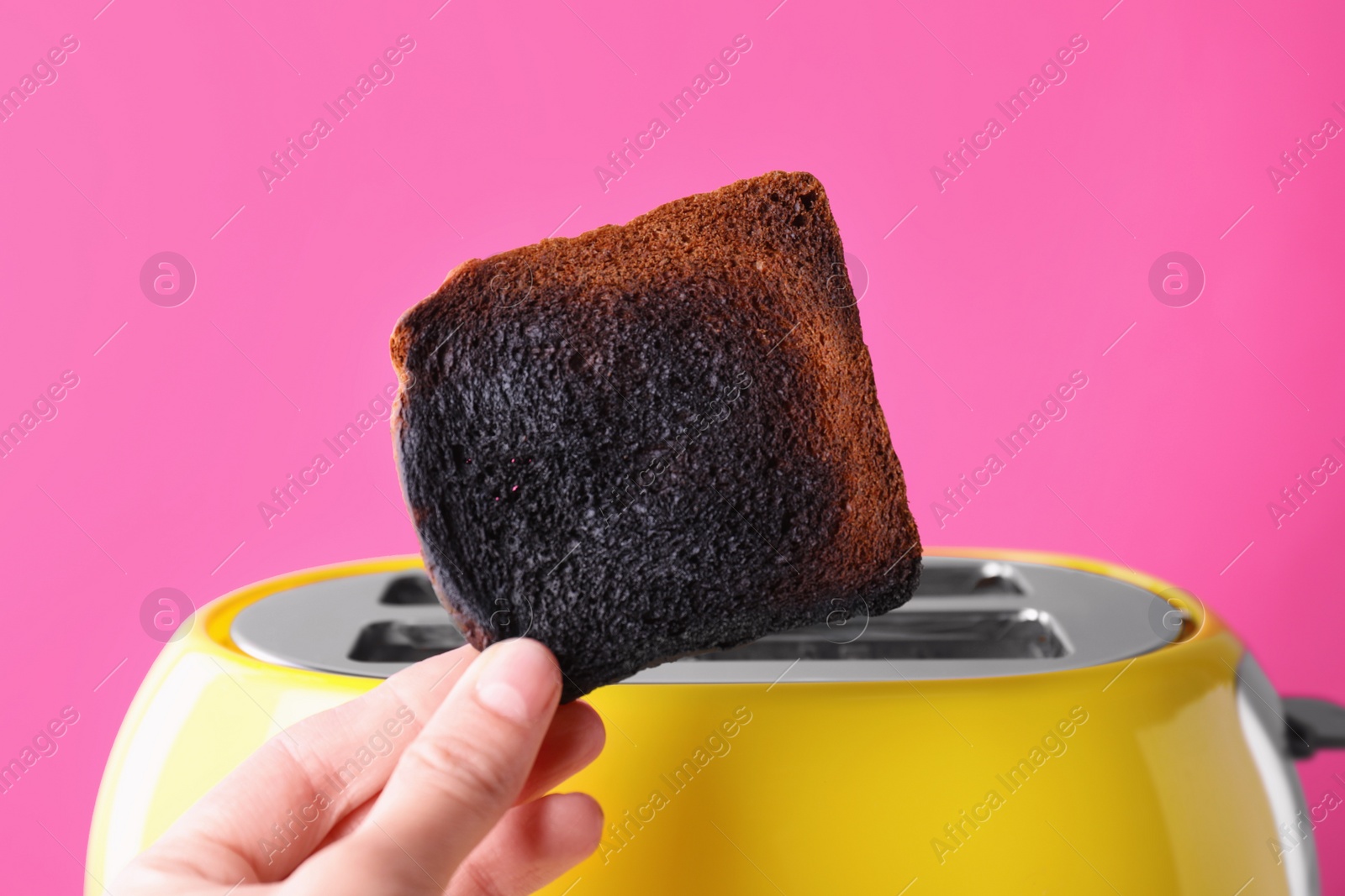 Photo of Woman holding burnt bread near toaster against pink background, closeup