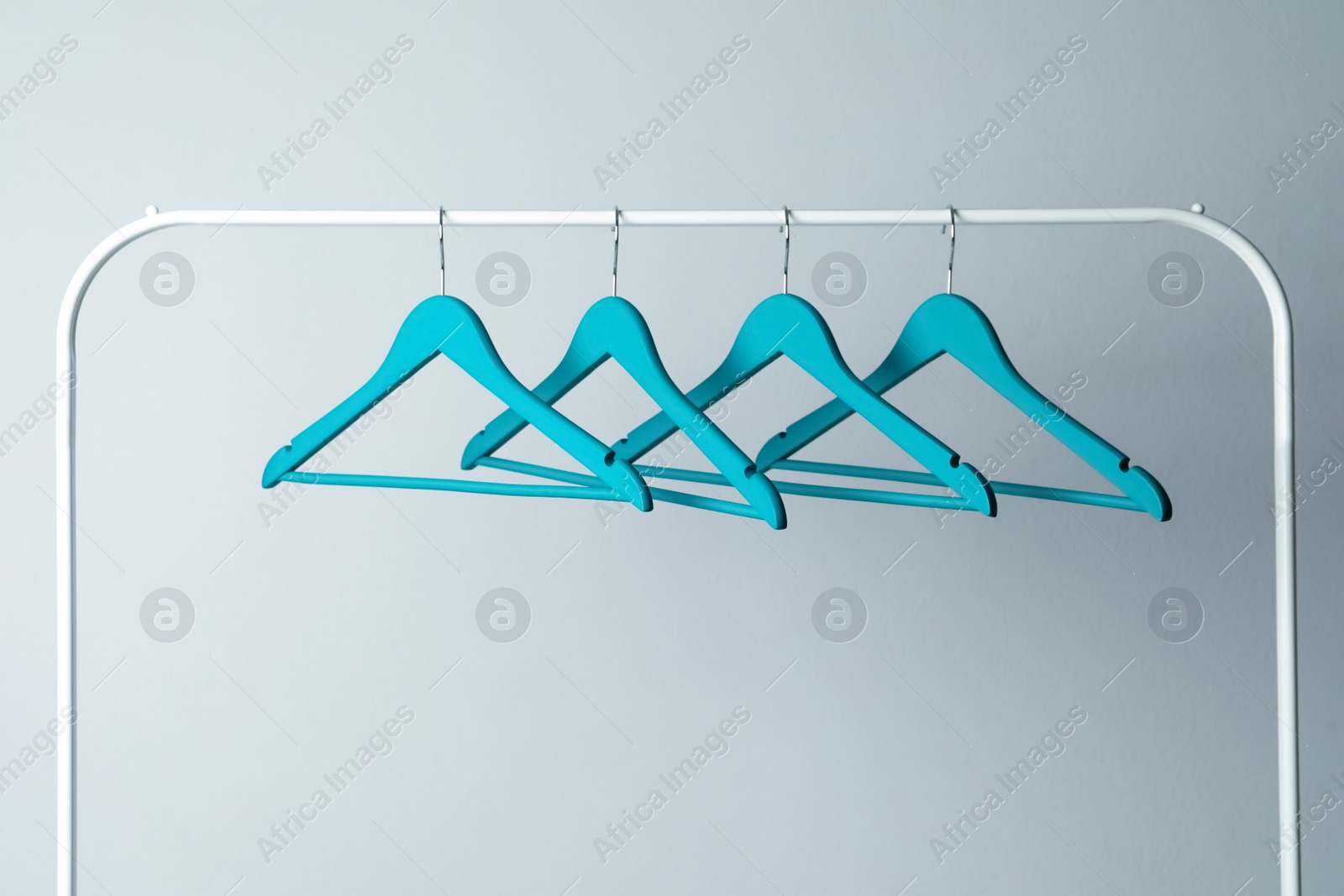 Photo of Empty turquoise clothes hangers on metal rack against light grey background