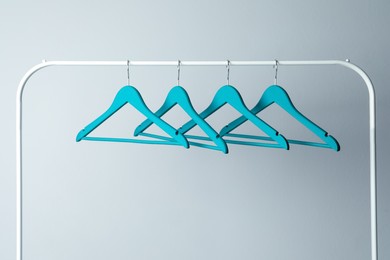 Photo of Empty turquoise clothes hangers on metal rack against light grey background
