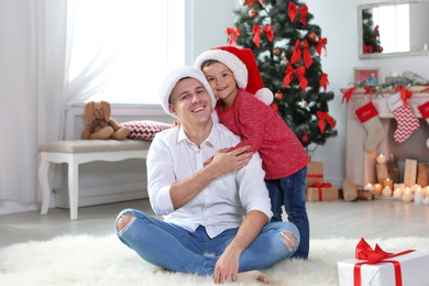 Photo of Father and child in Santa hats celebrating Christmas at home