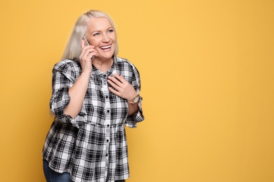 Mature woman talking on mobile phone against color background