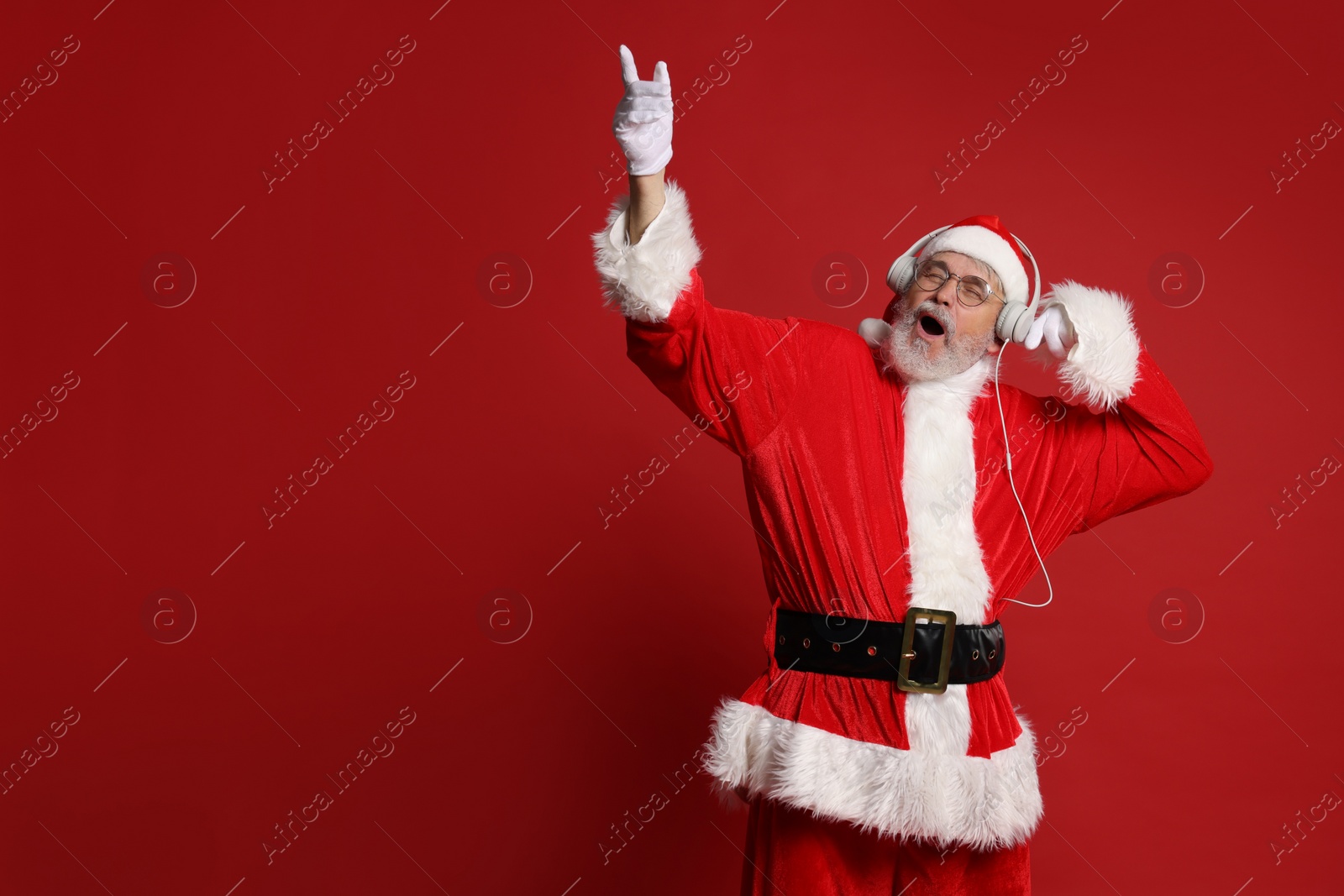 Photo of Merry Christmas. Santa Claus in headphones listening to music and singing on red background, space for text
