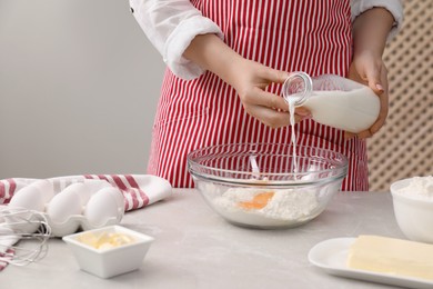 Photo of Preparing tasty baklava. Woman pouring milk into bowl with flour and eggs at light grey table, closeup