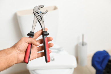 Photo of Professional plumber holding pliers against toilet bowl in bathroom, closeup