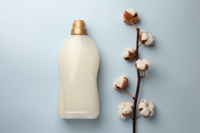 Photo of Bottle of fabric softener and branch with fluffy cotton flowers on light background, flat lay
