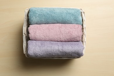 Wicker basket with clean soft towels on wooden table, top view