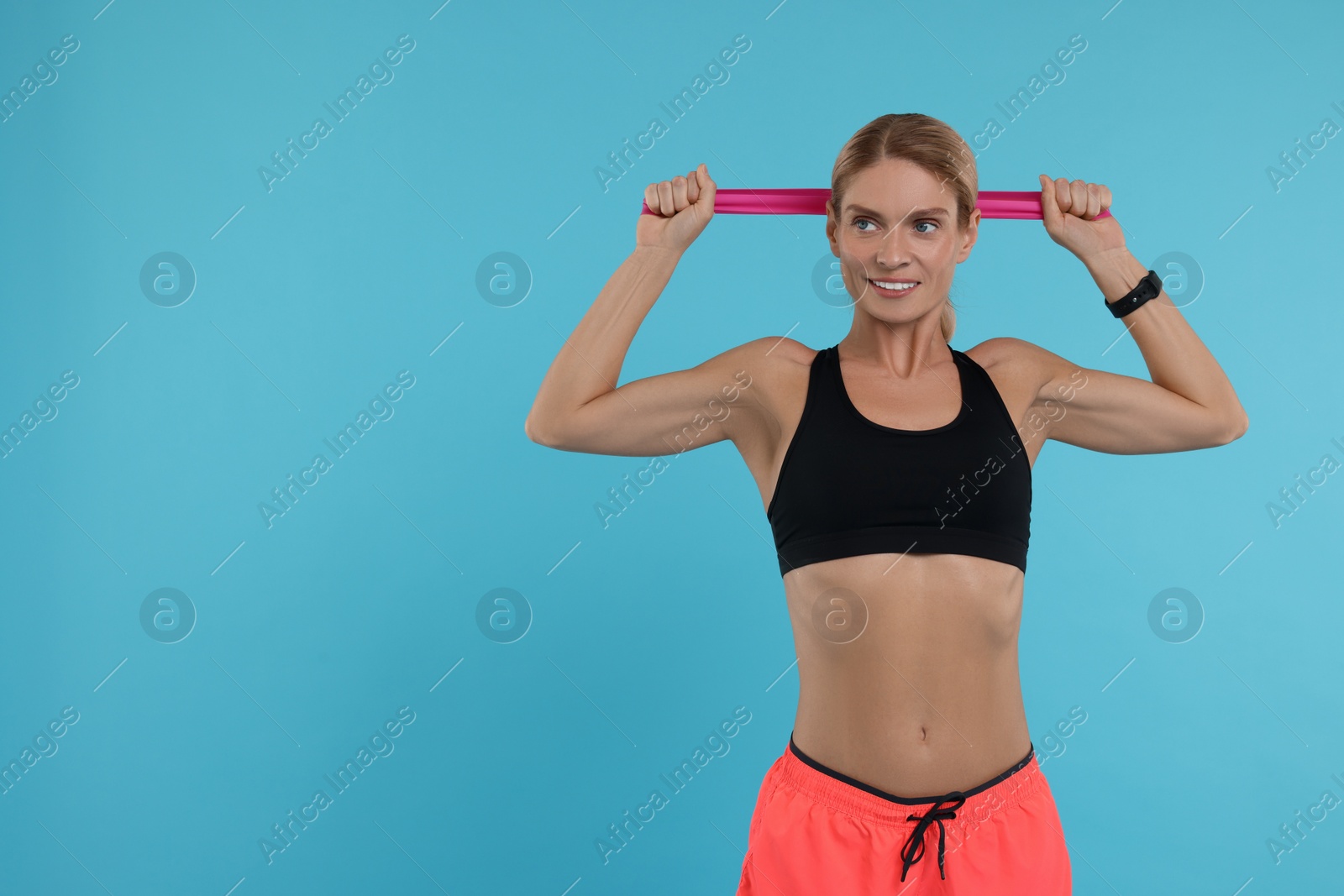 Photo of Woman exercising with elastic resistance band on light blue background. Space for text