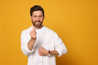 Photo of Smiling bearded man doing finger heart on orange background. Space for text