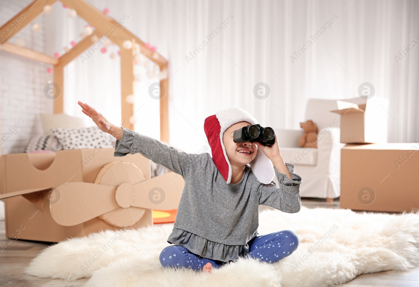 Photo of Cute little girl playing with binoculars and cardboard airplane in bedroom
