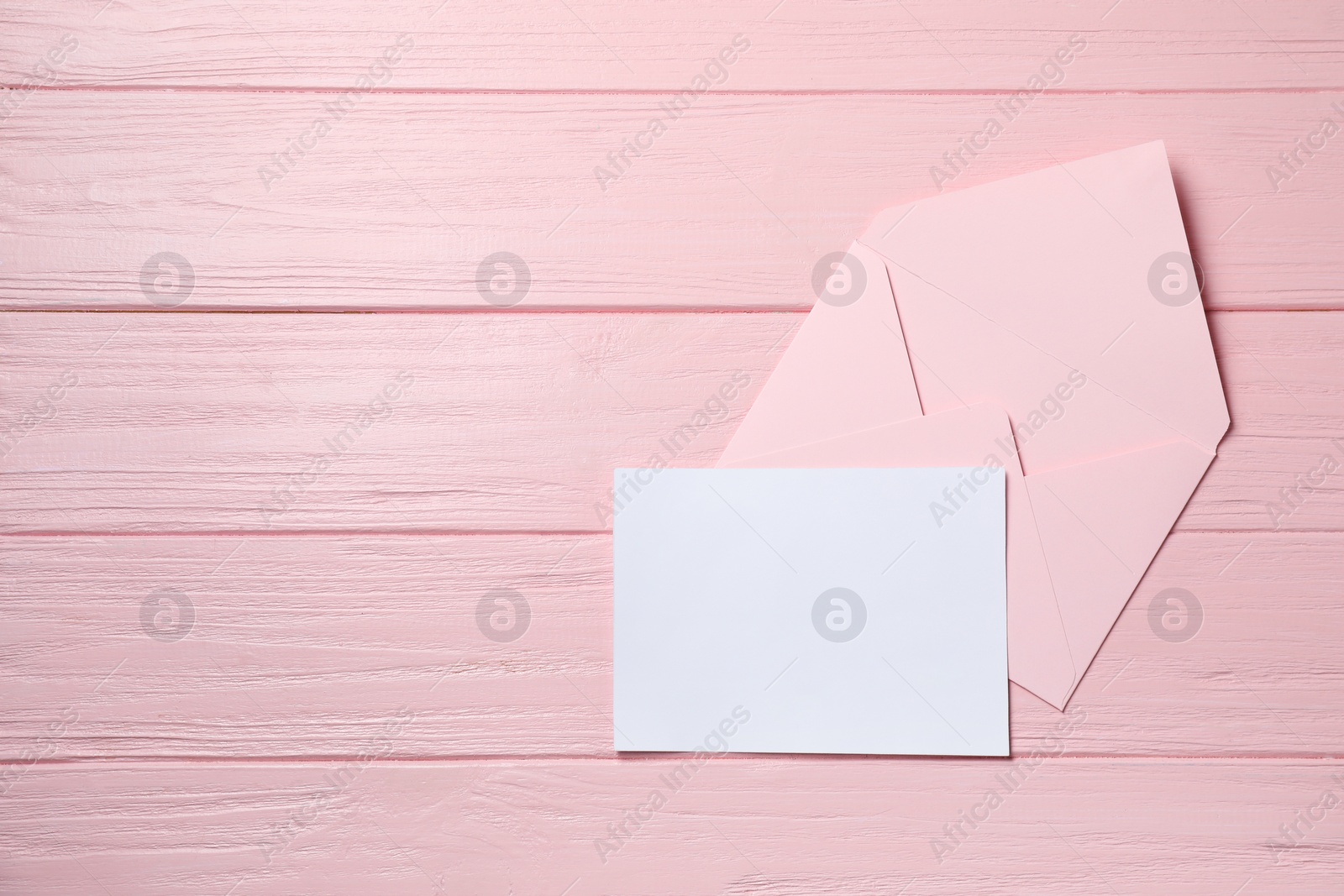 Photo of Blank sheet of paper and letter envelope on pink wooden table, top view. Space for text