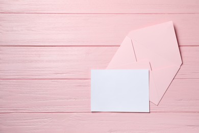 Photo of Blank sheet of paper and letter envelope on pink wooden table, top view. Space for text