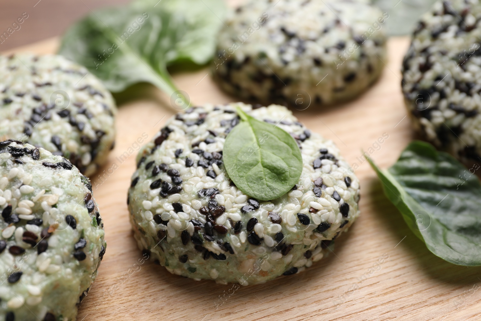 Photo of Tasty vegan cutlets with sesame seeds and spinach on wooden table, closeup