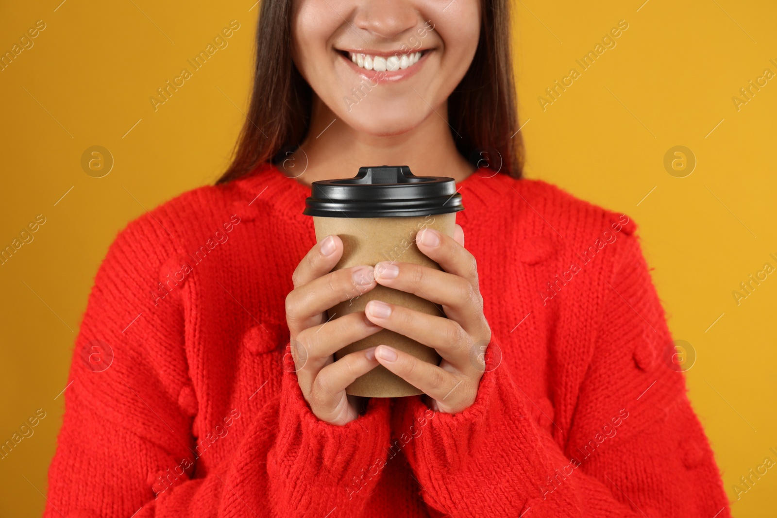 Photo of Happy beautiful woman with paper cup of mulled wine on yellow background, closeup