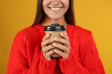 Happy beautiful woman with paper cup of mulled wine on yellow background, closeup