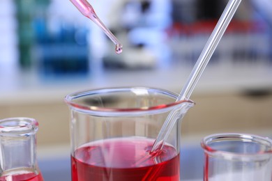 Laboratory analysis. Dripping red liquid into beaker on table, closeup