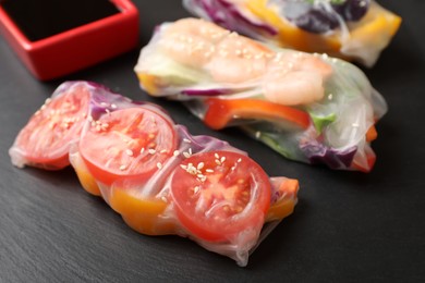 Delicious rolls wrapped in rice paper served on black table, closeup