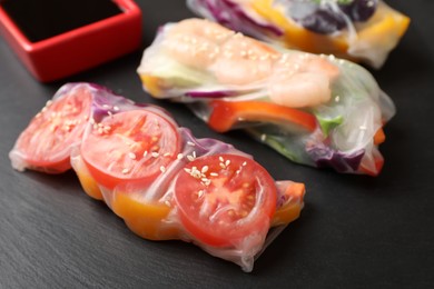 Photo of Delicious rolls wrapped in rice paper served on black table, closeup