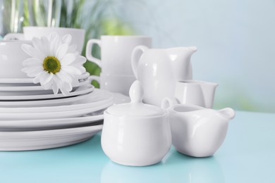 Photo of Set of clean dishware and flower on light blue table, closeup
