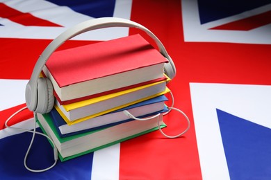 Photo of Learning foreign language. Different books and headphones on flag of United Kingdom, space for text