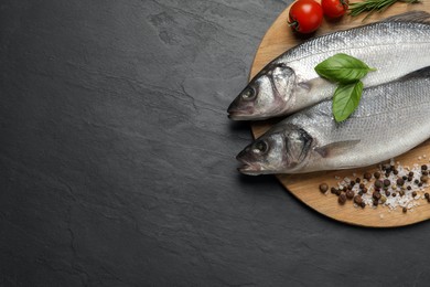 Photo of Sea bass fish and ingredients on black table, top view. Space for text
