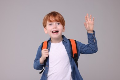 Photo of Happy schoolboy waving hello on grey background