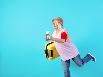 Senior woman with suitcase and passport running on color background. Space for text