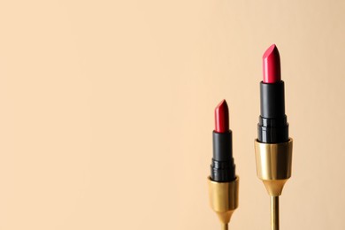 Beautiful glossy lipsticks on beige background, space for text
