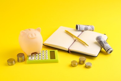 Photo of Financial savings. Piggy bank, money, calculator and stationery on yellow background