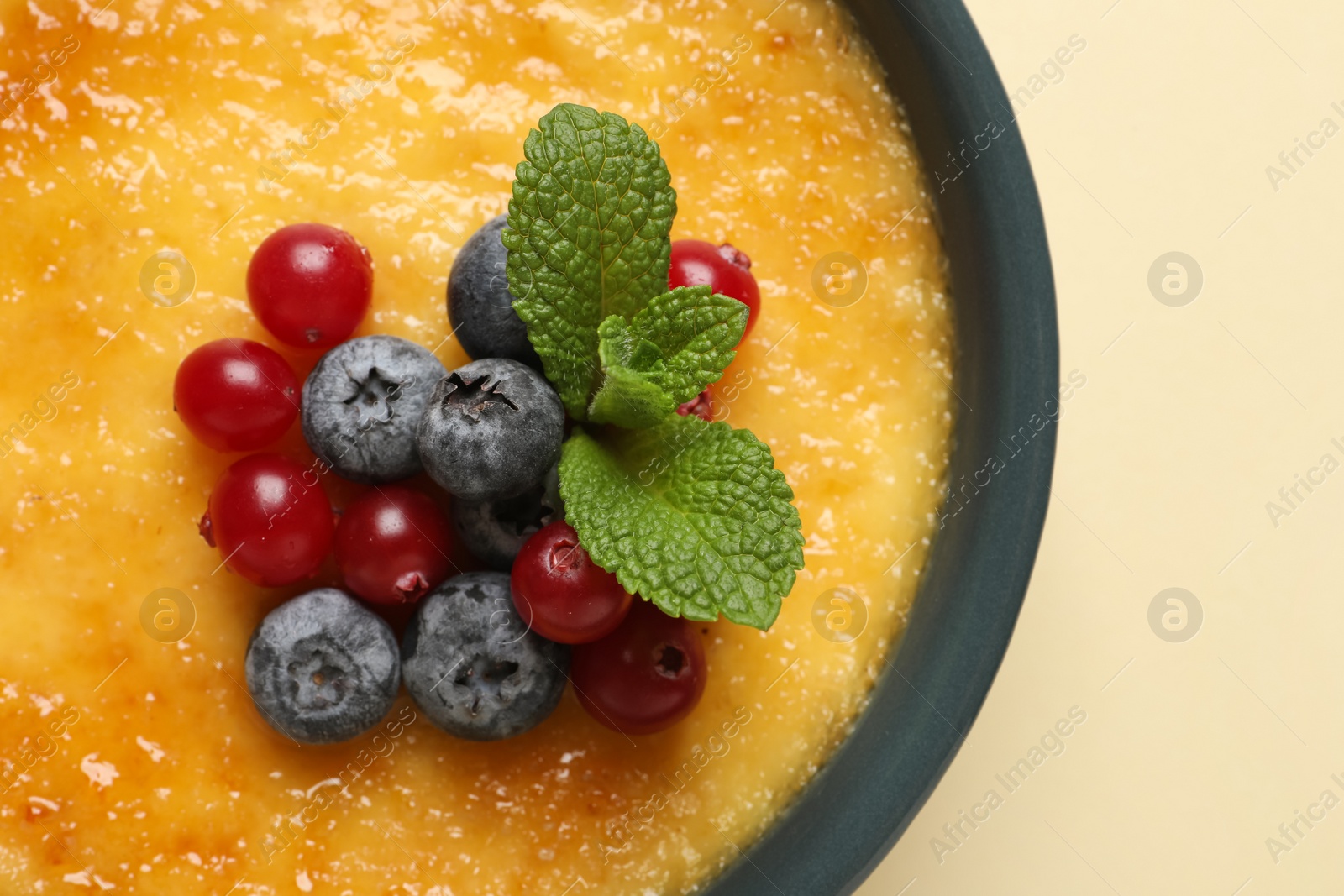 Photo of Delicious creme brulee with fresh berries on beige background, closeup