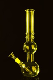 Photo of Glass bong on black background, toned in yellow. Smoking device