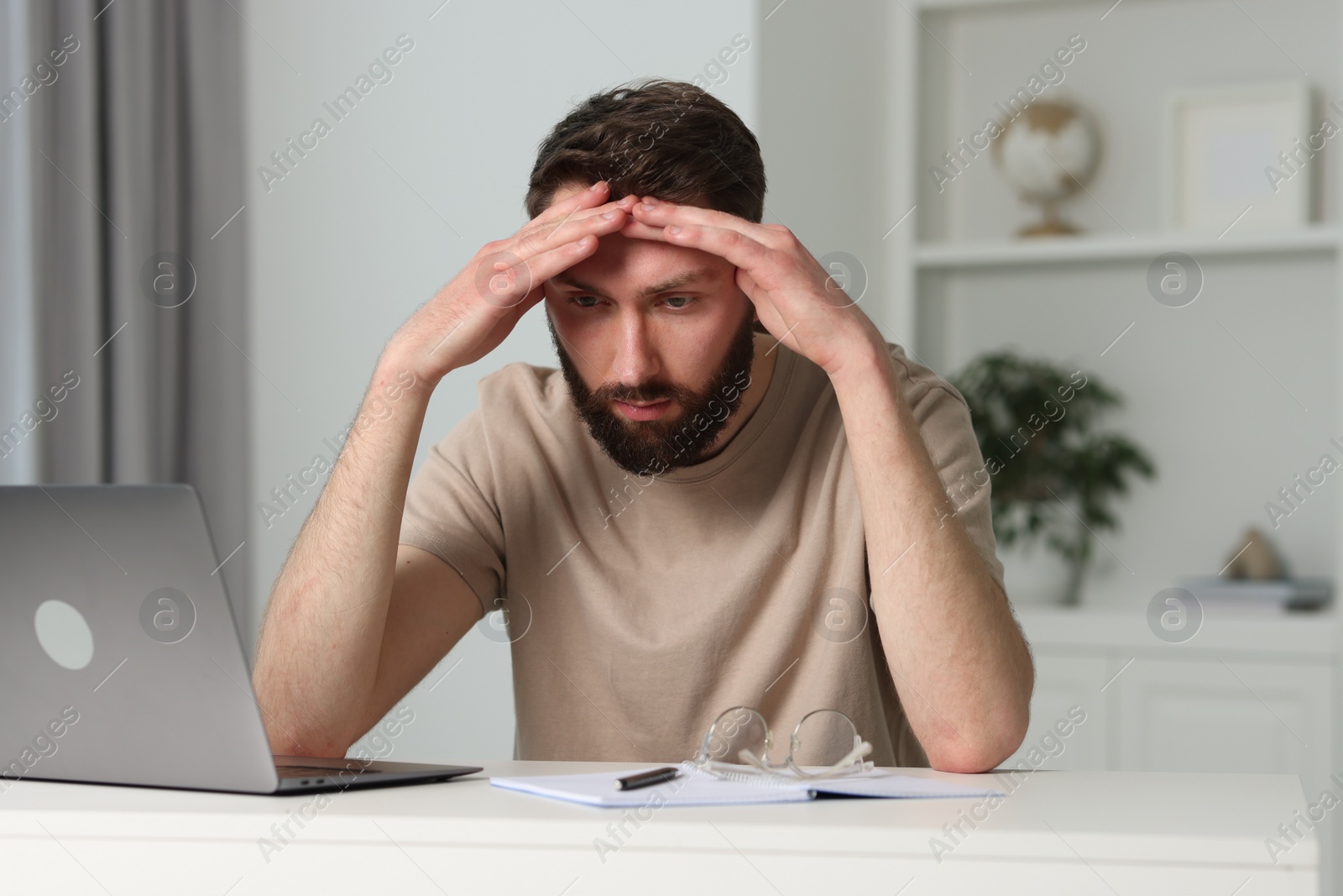 Photo of Overwhelmed man sitting with laptop at table indoors