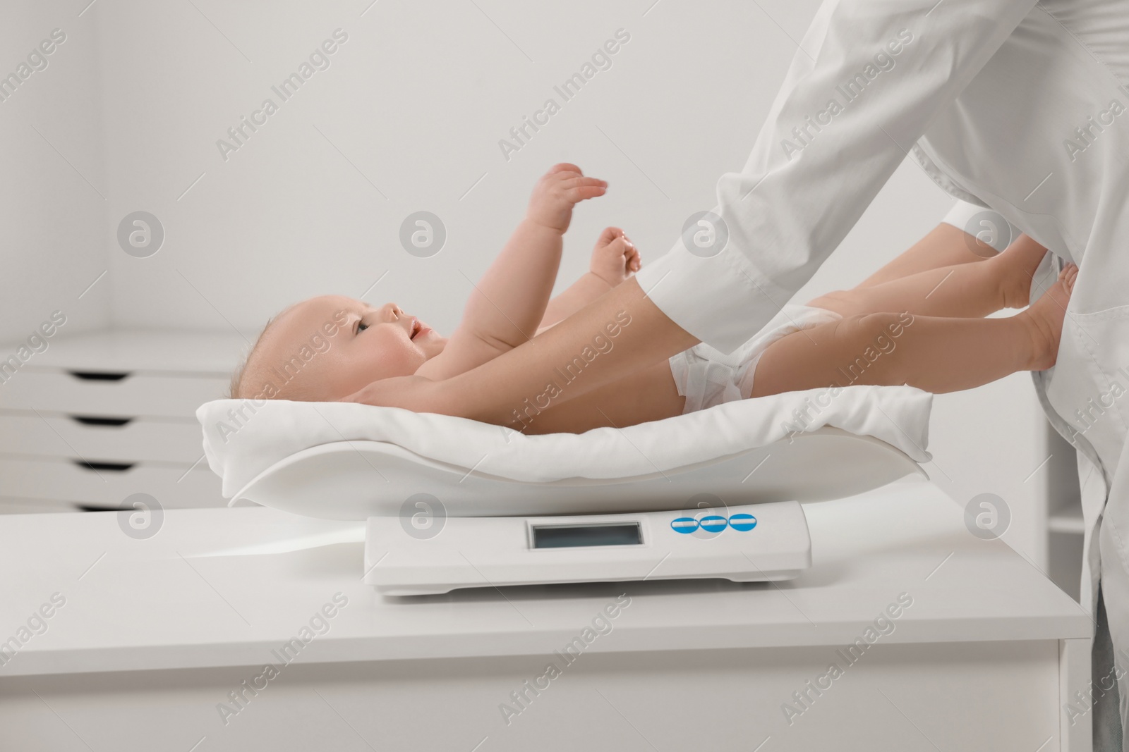 Photo of Pediatrician weighting cute little baby in clinic, closeup