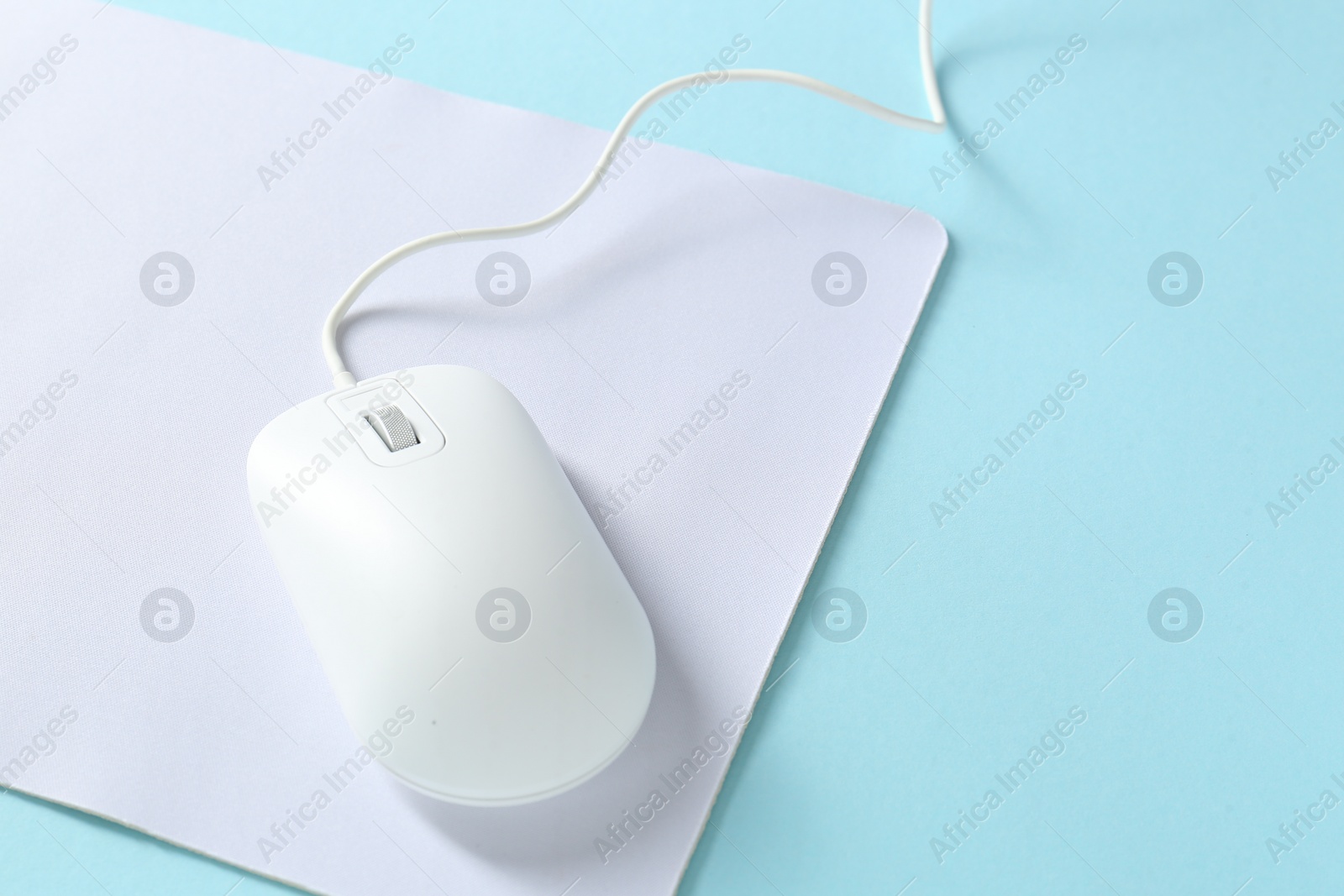Photo of Wired mouse and mousepad on light blue background, space for text