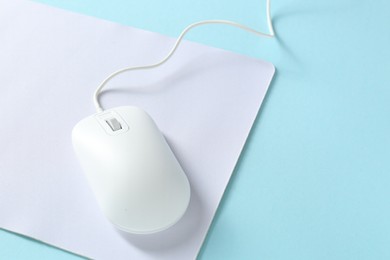 Photo of Wired mouse and mousepad on light blue background, space for text