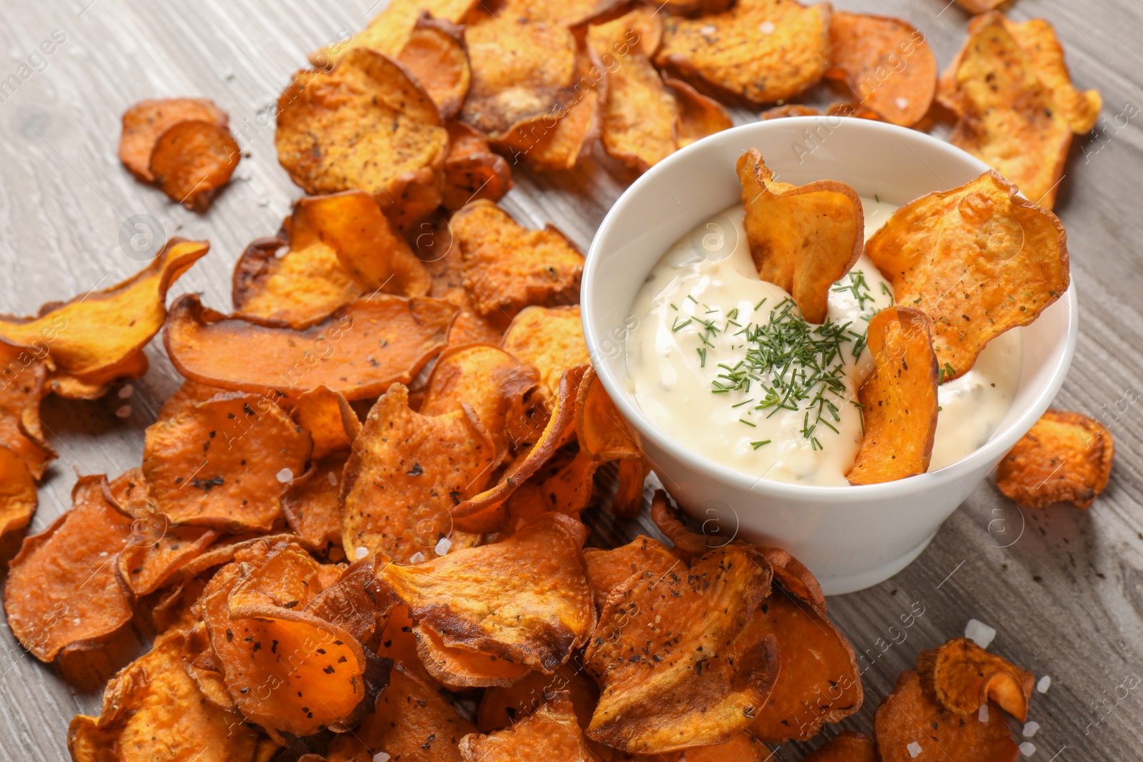 Photo of Sweet potato chips and bowl of sauce on wooden background