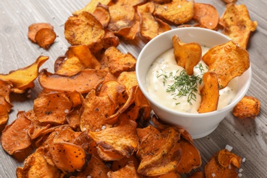 Photo of Sweet potato chips and bowl of sauce on wooden background