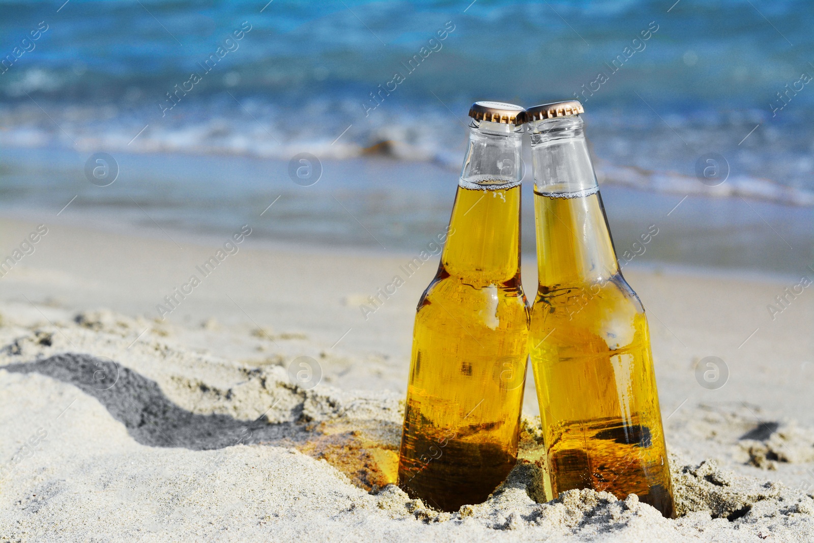 Photo of Bottles of cold beer on sandy beach near sea, space for text