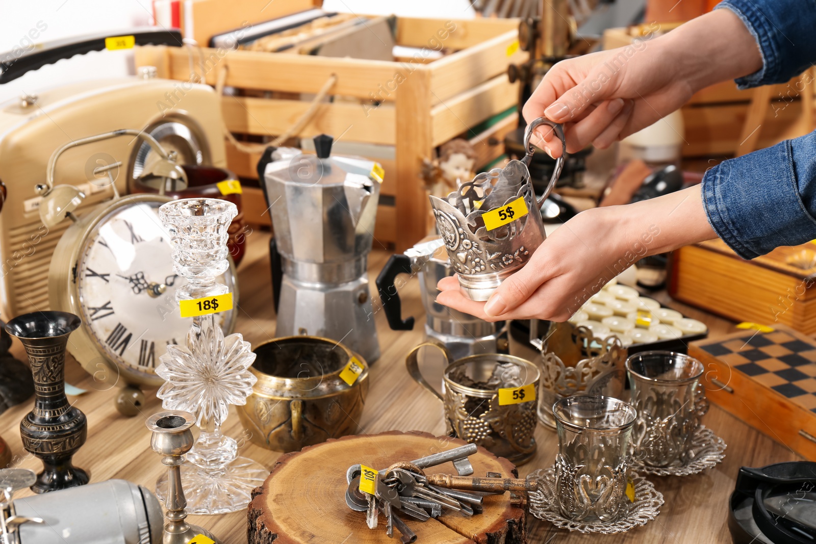 Photo of Woman holding vintage metal cup near table with different stuff, closeup. Garage sale
