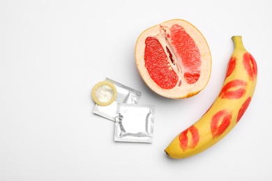 Photo of Condoms, cut grapefruit and banana with lipstick kiss marks on white background, flat lay. Safe sex