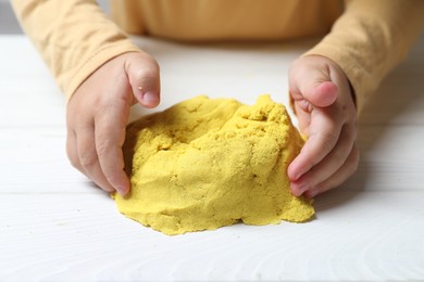 Photo of Little child playing with yellow kinetic sand at white wooden table, closeup