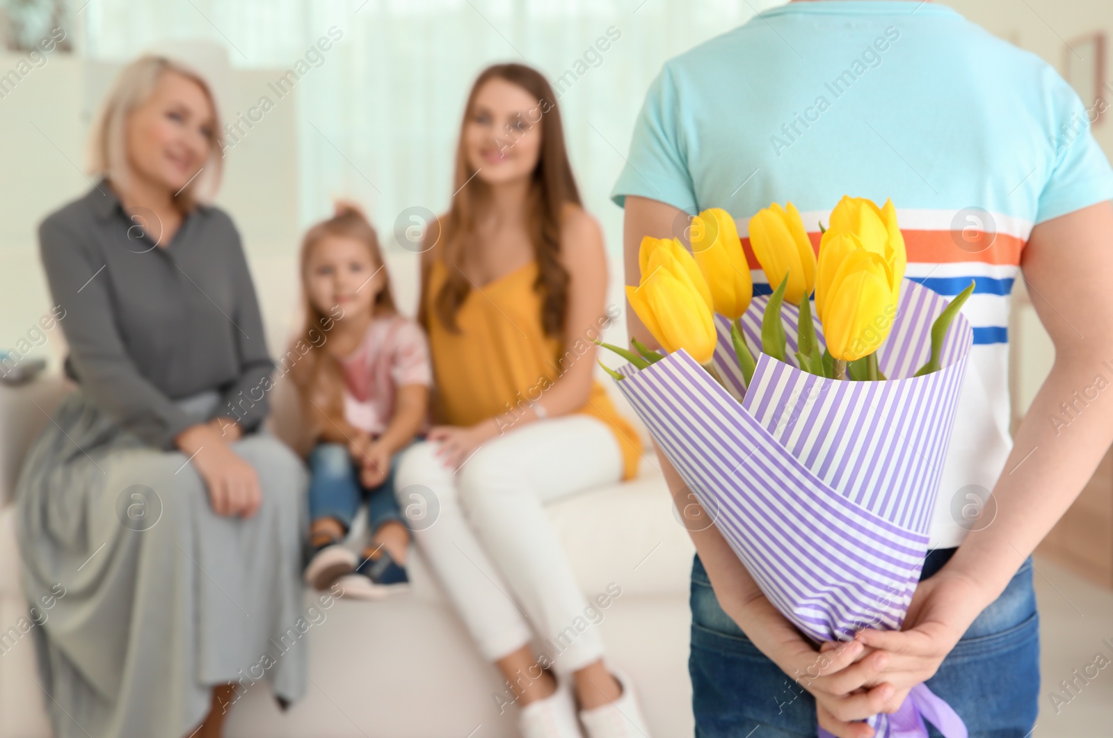 Photo of Little boy hiding tulip bouquet for family behind his back at home